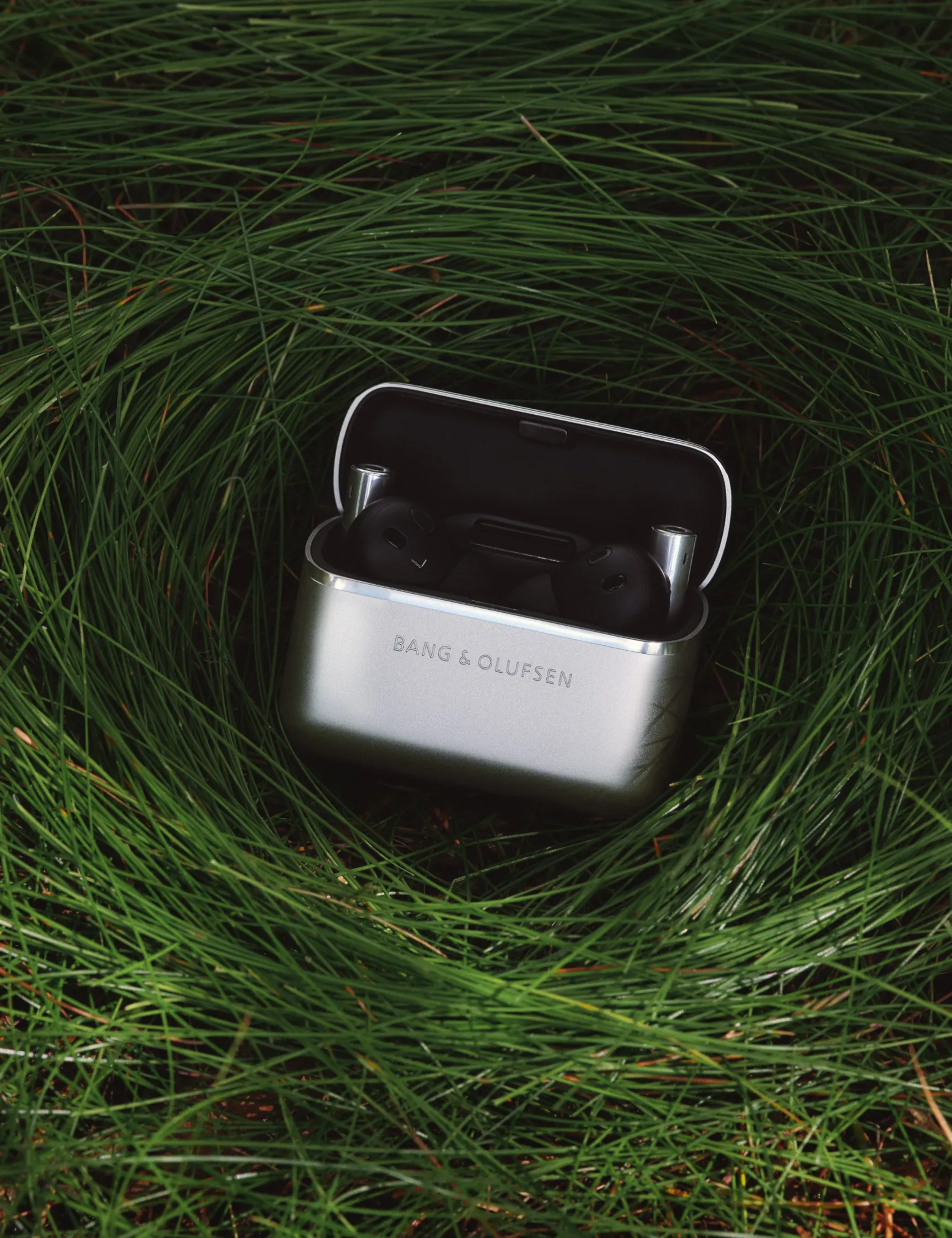 Beo Grace Charging case opened, showing the earphones inside on the grass