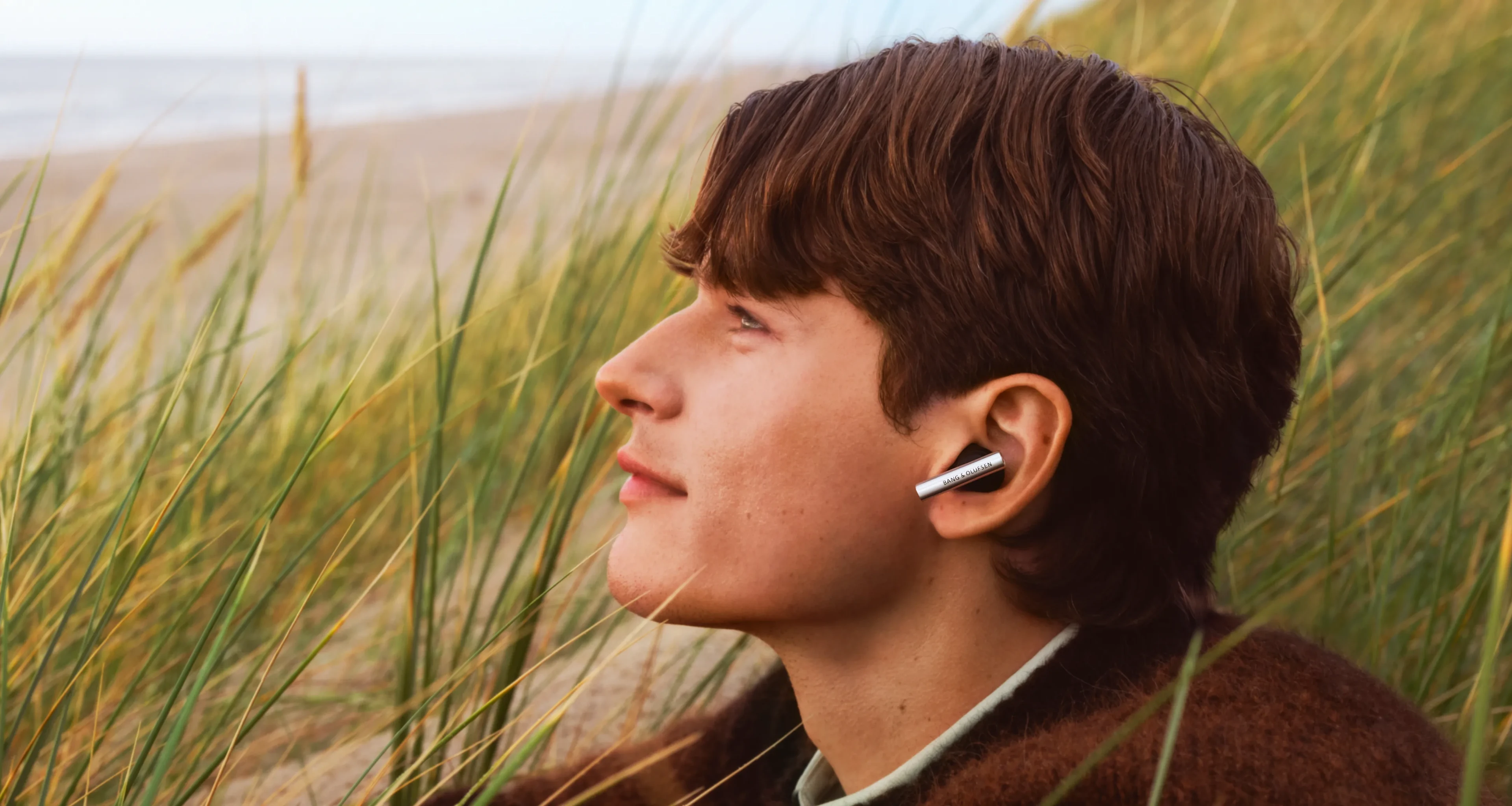 Side face of a man wearing Beo Grace Aluminium color, sitting outside near the ocean gazing somewhere