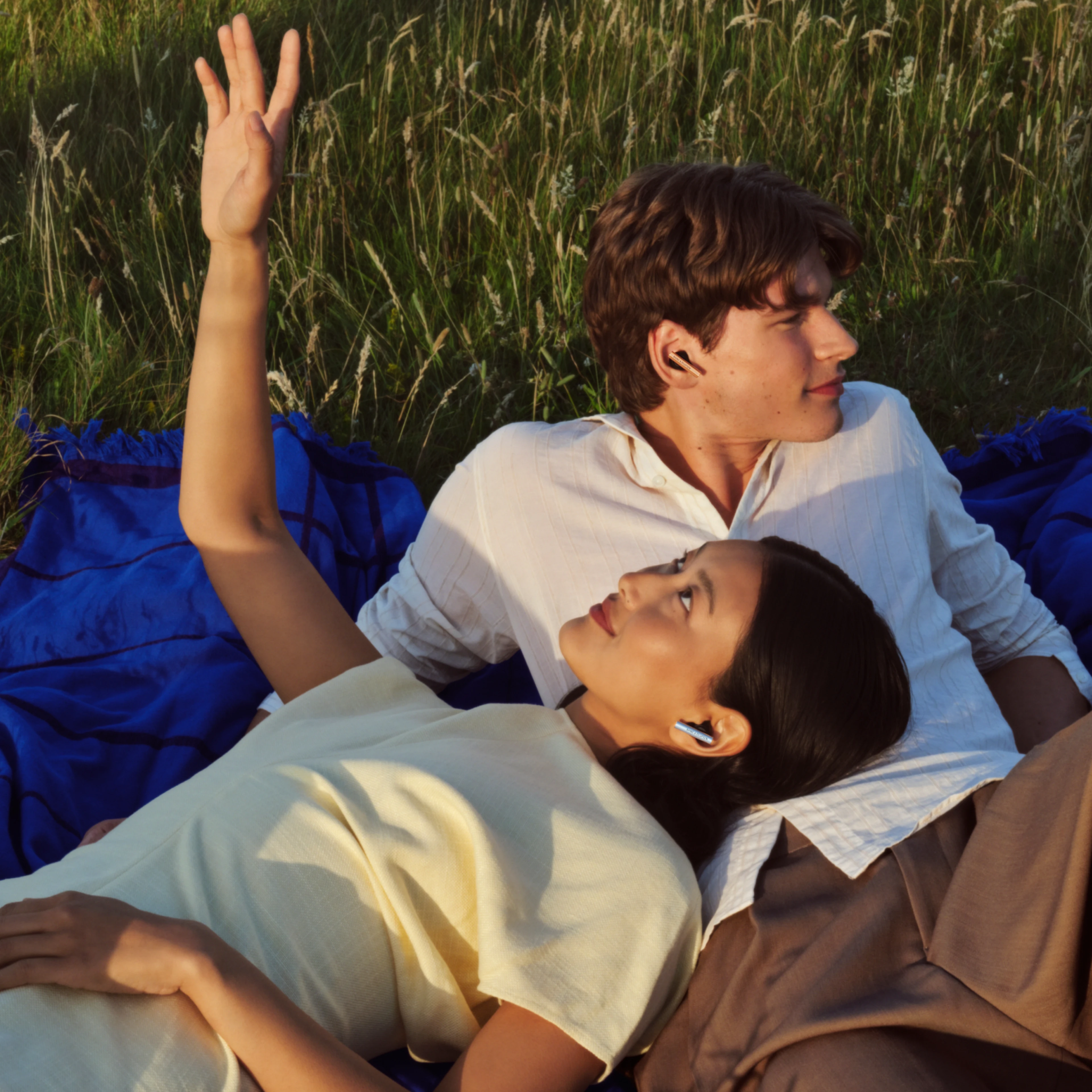 A couple lying down together on the grass wearing Beo Grace earbuds and enjoying their time